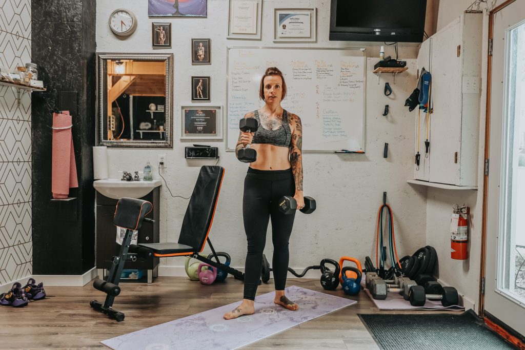 Woman with tattoos working out, hammer curling dumbells in home fitness studio