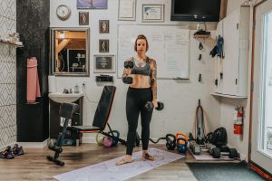 Woman with tattoos working out, hammer curling dumbells in home fitness studio