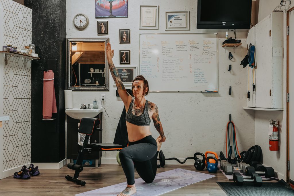 Woman with tattoos stretching, doing yoga in home fitness studio